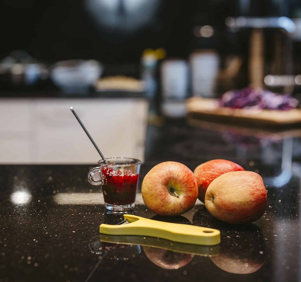 Fresh apples, yellow peeler, and glass of red jam on black kitchen counter