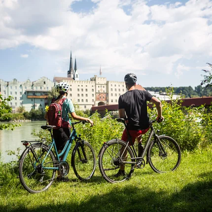 Twee fietsers met helmen kijken uit op gebouwen langs de rivier op een zonnige dag