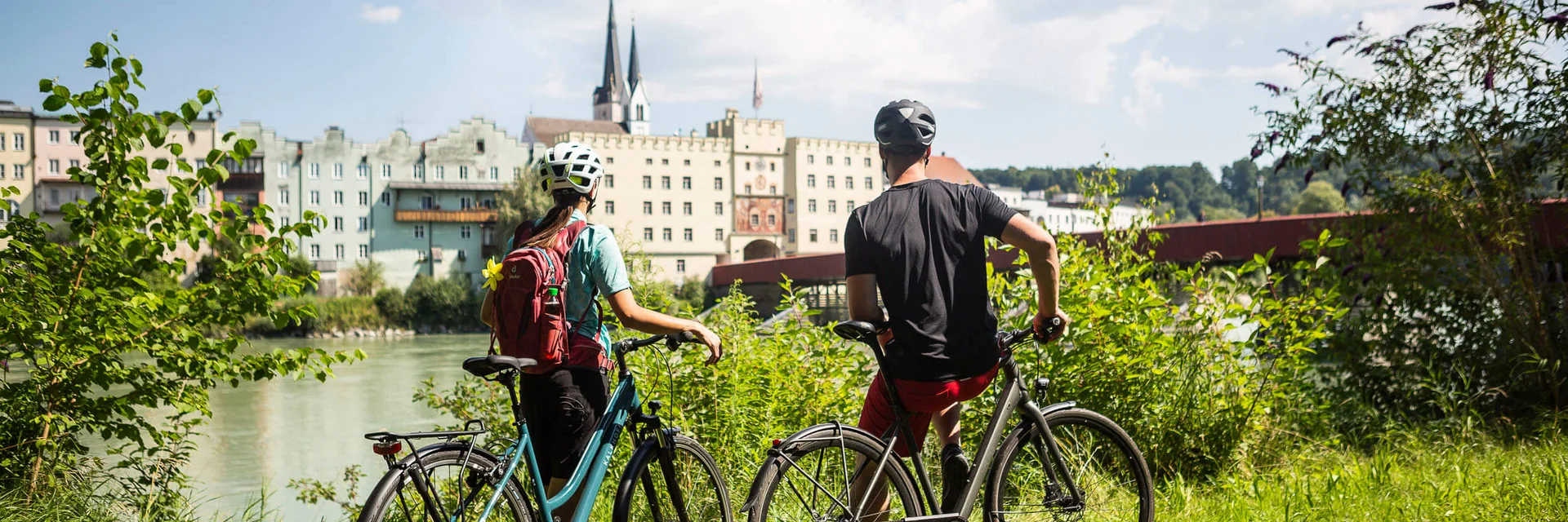 Twee fietsers met helmen kijken uit op gebouwen langs de rivier op een zonnige dag