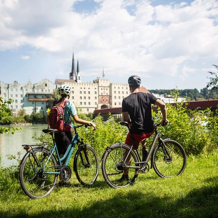 Two cyclists wearing helmets overlooking riverside buildings on a sunny day