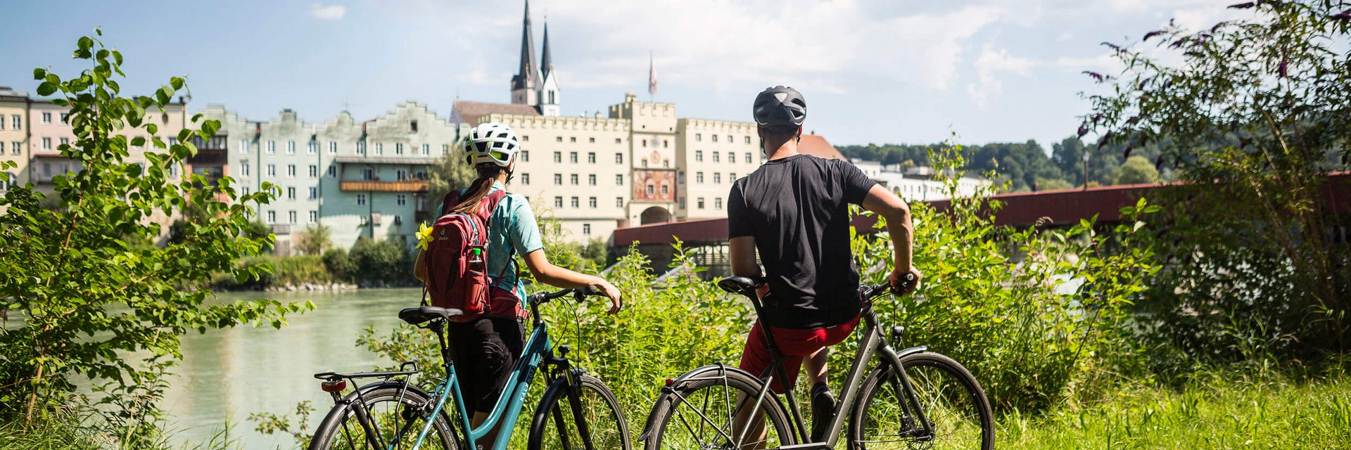 Two cyclists wearing helmets overlooking riverside buildings on a sunny day