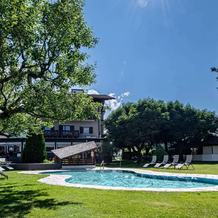 Sonniger Garten mit Pool und Liegestühlen unter Bäumen