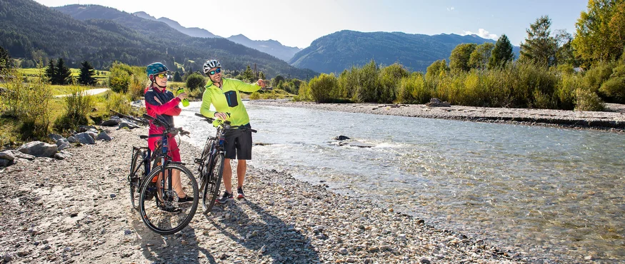 Two cyclists taking a break by riverbank in the mountains