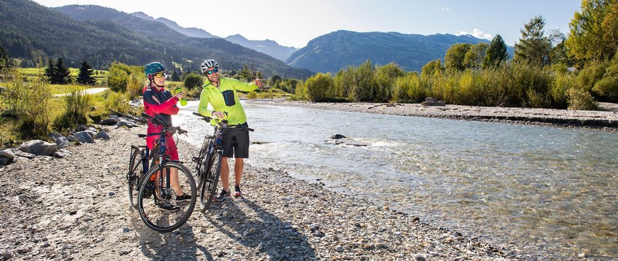 Two cyclists taking a break by riverbank in the mountains