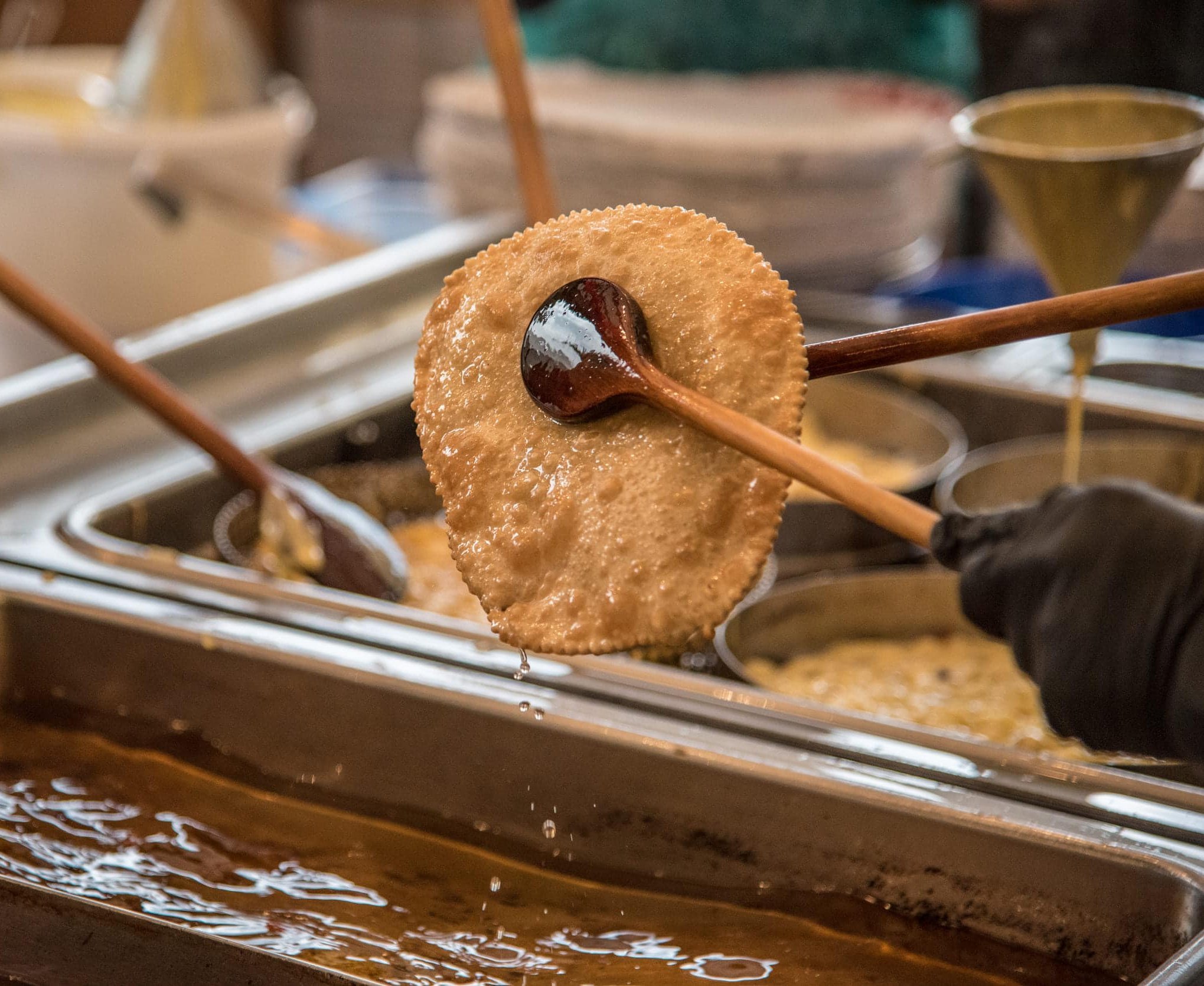 Person frying thin dough flatbread in hot oil using wooden spoon