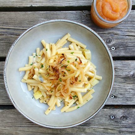Plate of cheesy noodles with fried onions and apple sauce on wooden table
