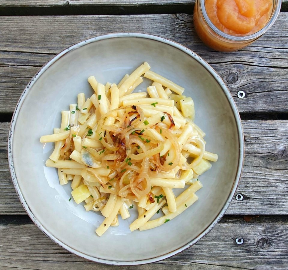 Plate of cheesy noodles with fried onions and apple sauce on wooden table