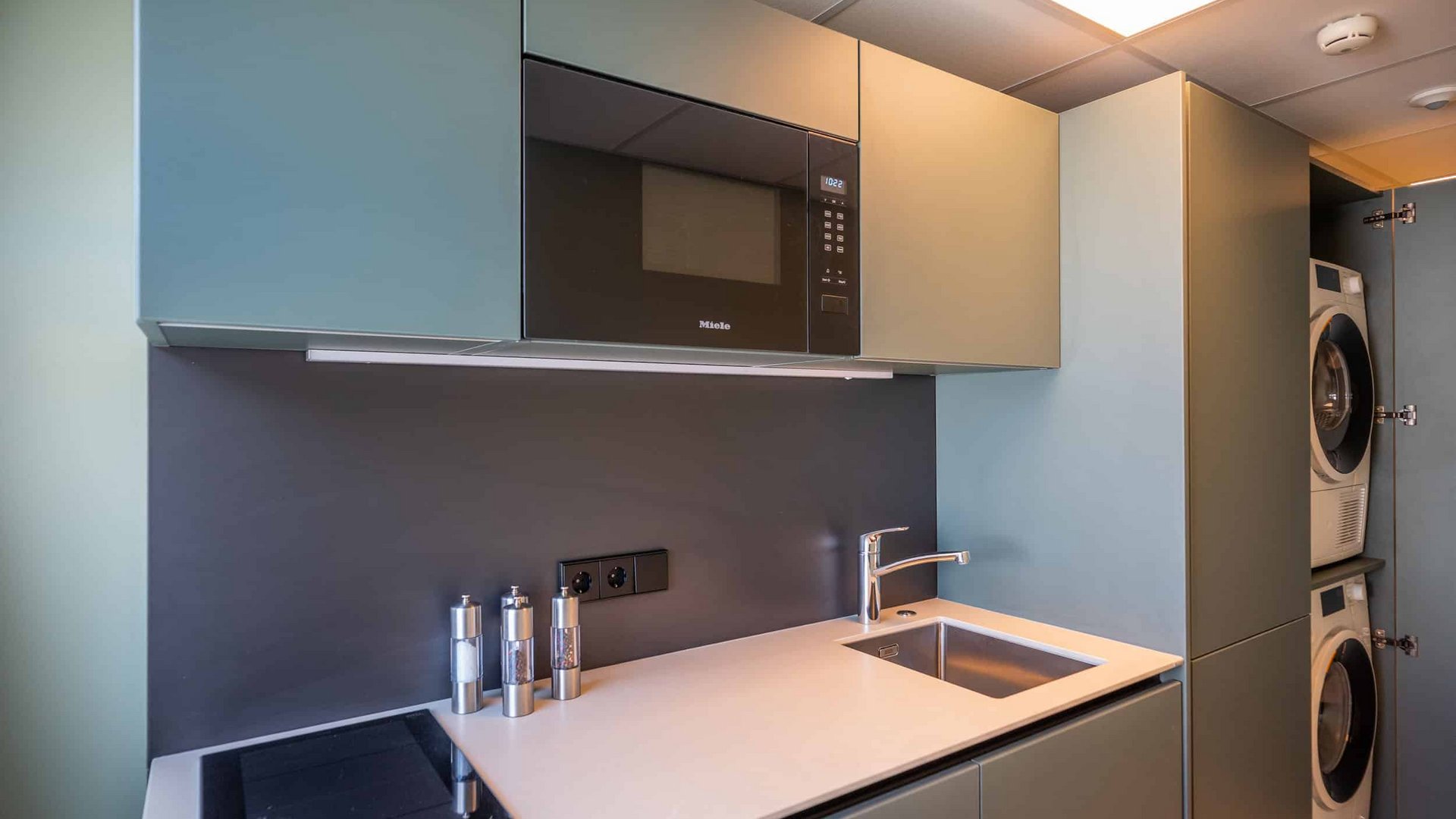 Modern kitchenette with microwave, stove, sink, and built-in washer and dryer