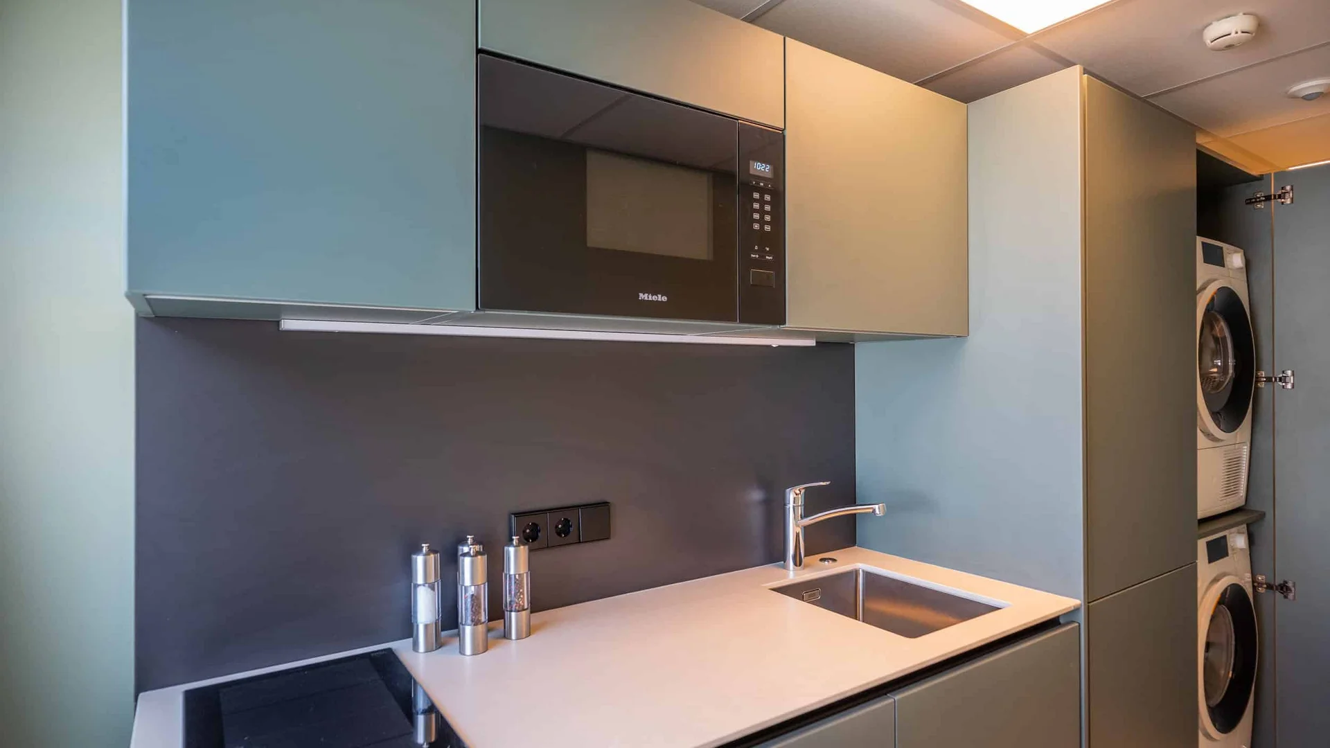 Moderne kitchenette met magnetron, fornuis, gootsteen en ingebouwde wasmachine en droger