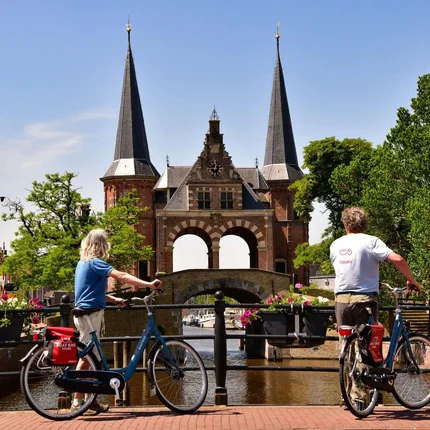 Twee fietsers kijken naar een historisch poort aan een gracht bij zonnig weer