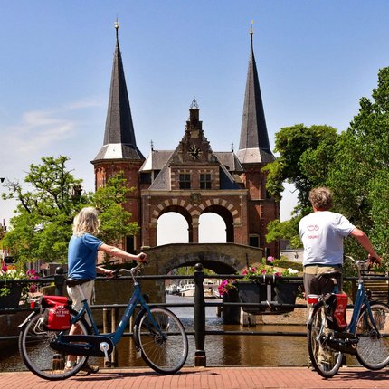 Two cyclists viewing a historic gate over a canal on a sunny day