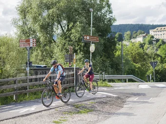 Dolomites region Kronplatz Two cyclists on a bike path in rural area with signs and mountains in background