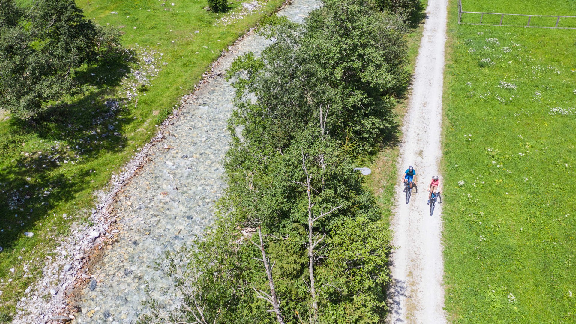 Two cyclists on a path next to a stream and green meadow