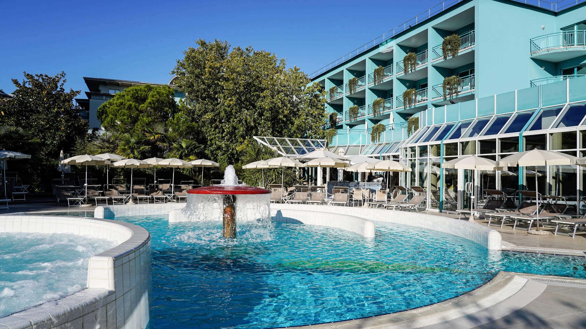 Pool with fountain and umbrellas next to blue hotel building