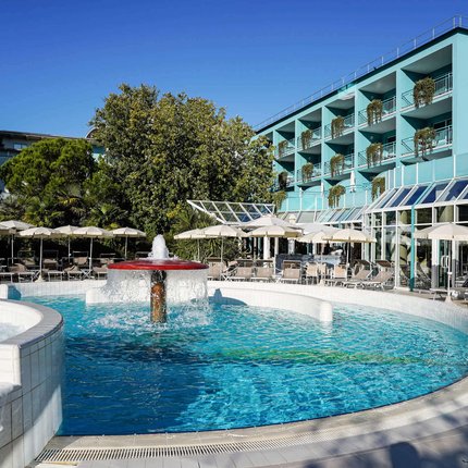 Pool with fountain and umbrellas next to blue hotel building