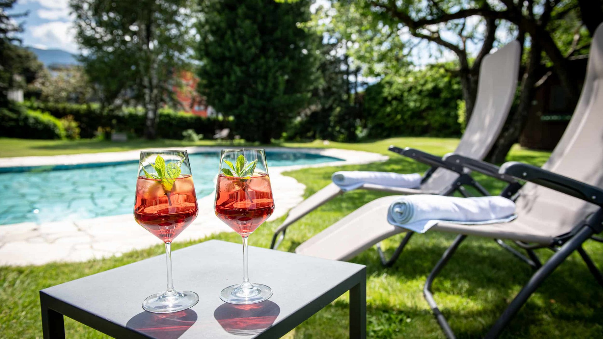 Two drinks on table near pool with lounge chairs in garden