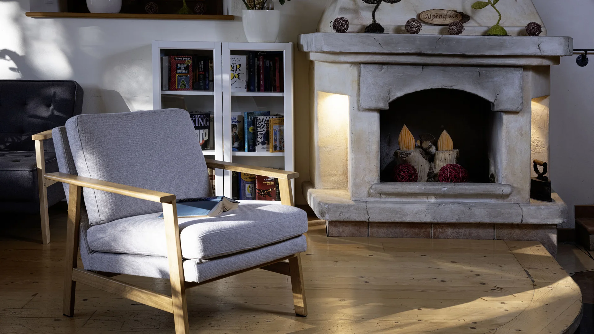 Light gray armchair beside stone fireplace in cozy living room