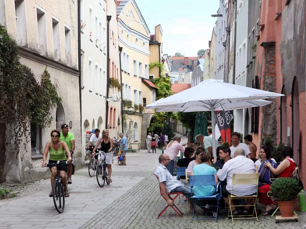 Radfahren ohne Höhenmeter-Stress im Quellenviertel © Burghauser Touristik Menschen beim Radfahren und Sitzen in einem Straßencafé in einer malerischen Altstadt