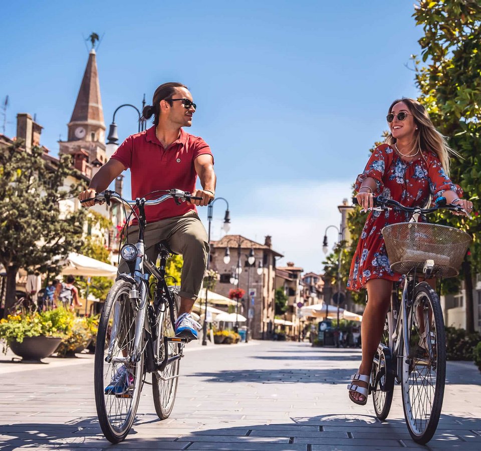 Paar fährt bei sonnigem Wetter mit Fahrrädern durch eine Altstadt