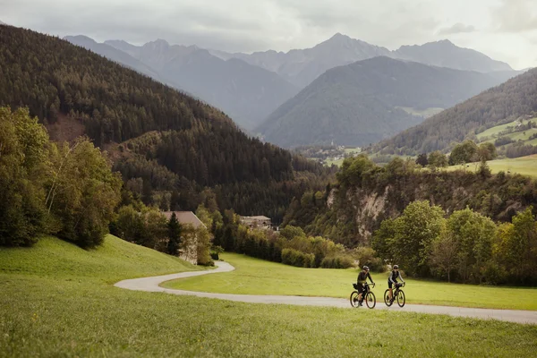 Italy Two cyclists on rural road in green mountain landscape under cloudy sky