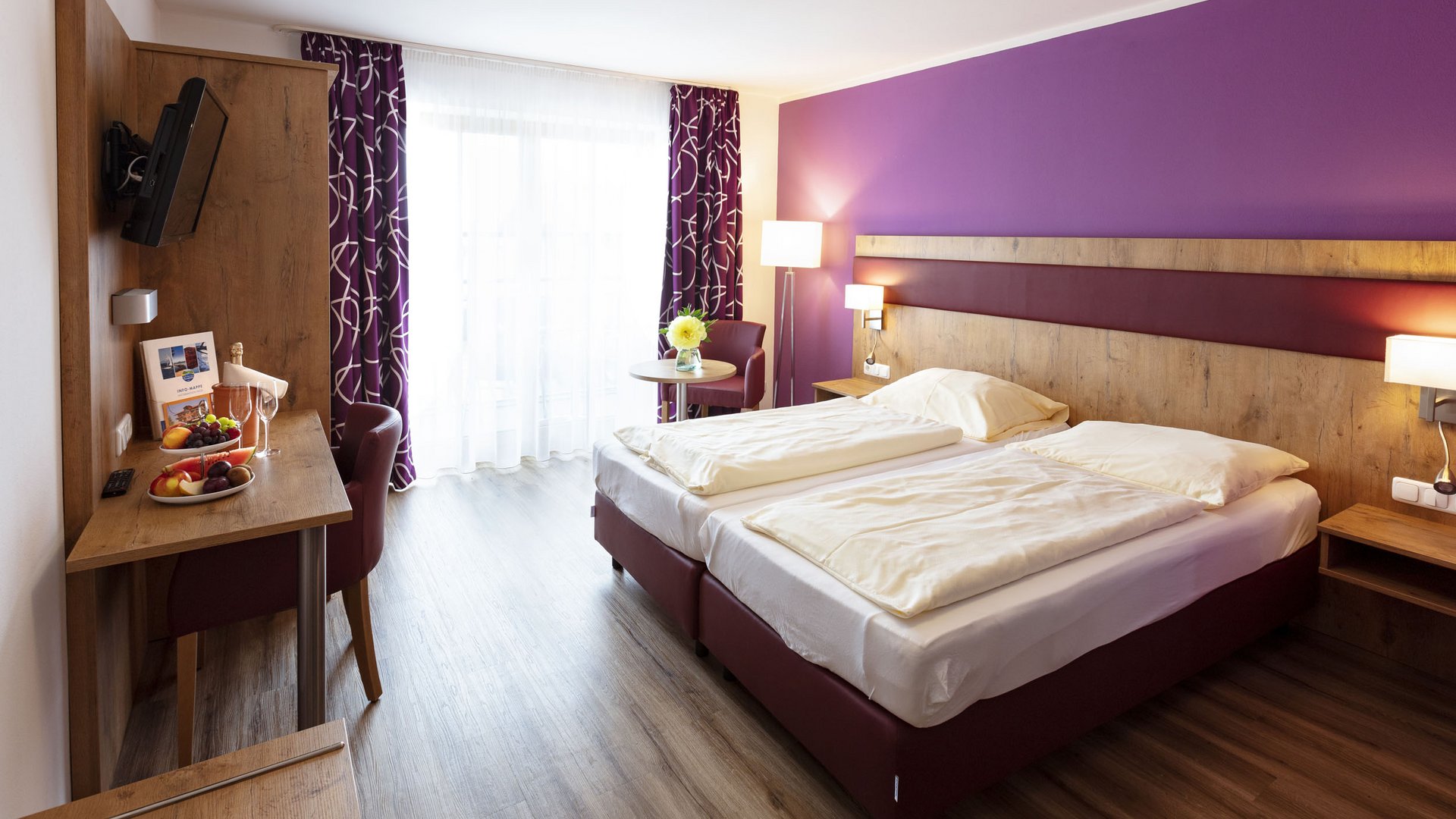 Modern hotel room with purple wall, double bed, and desk