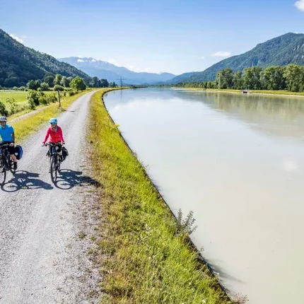 Zwei Radfahrer auf einem Weg entlang eines Flusses in den Bergen bei sonnigem Wetter