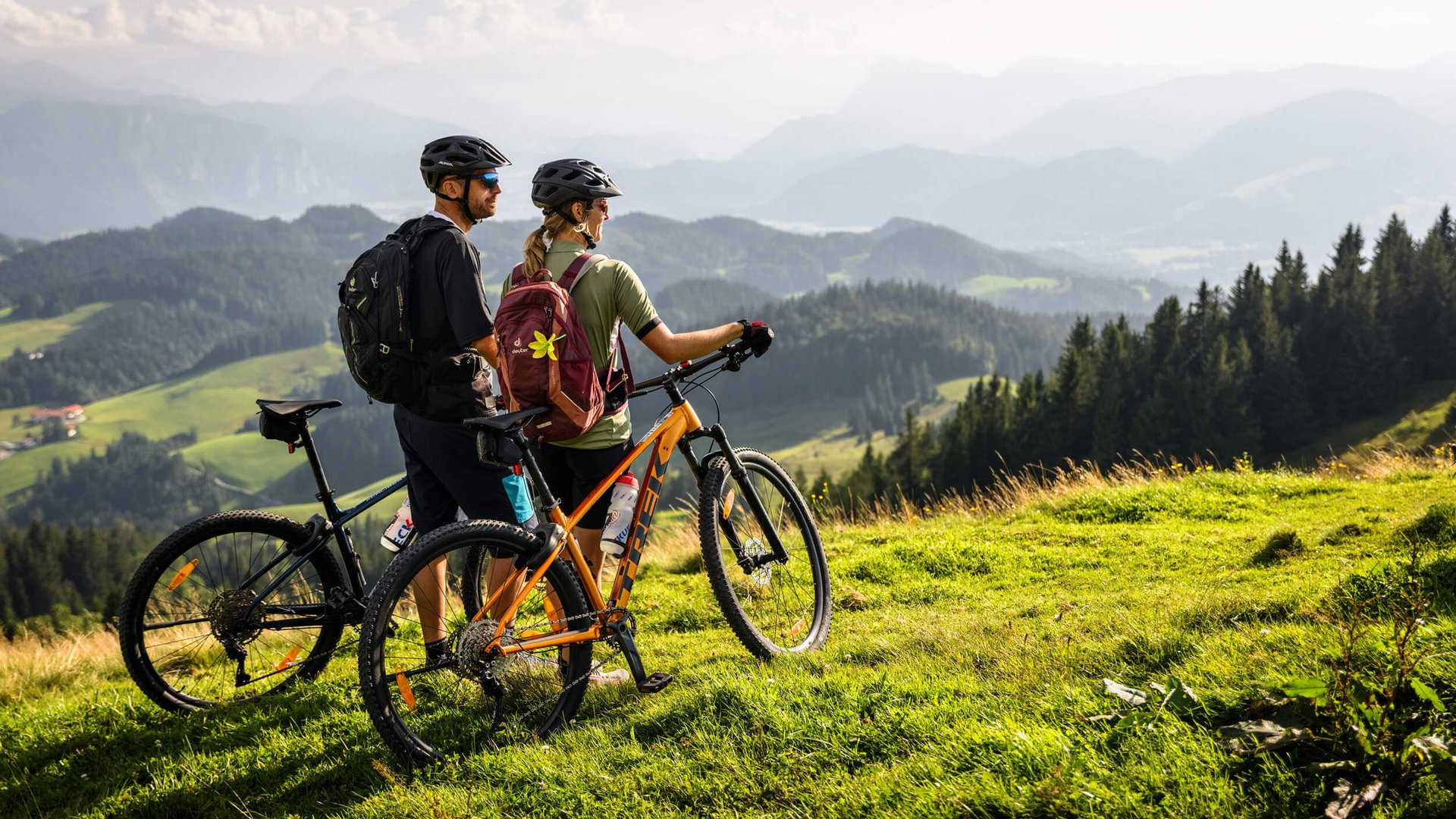 Two cyclists with helmets on a mountain meadow overlooking mountains