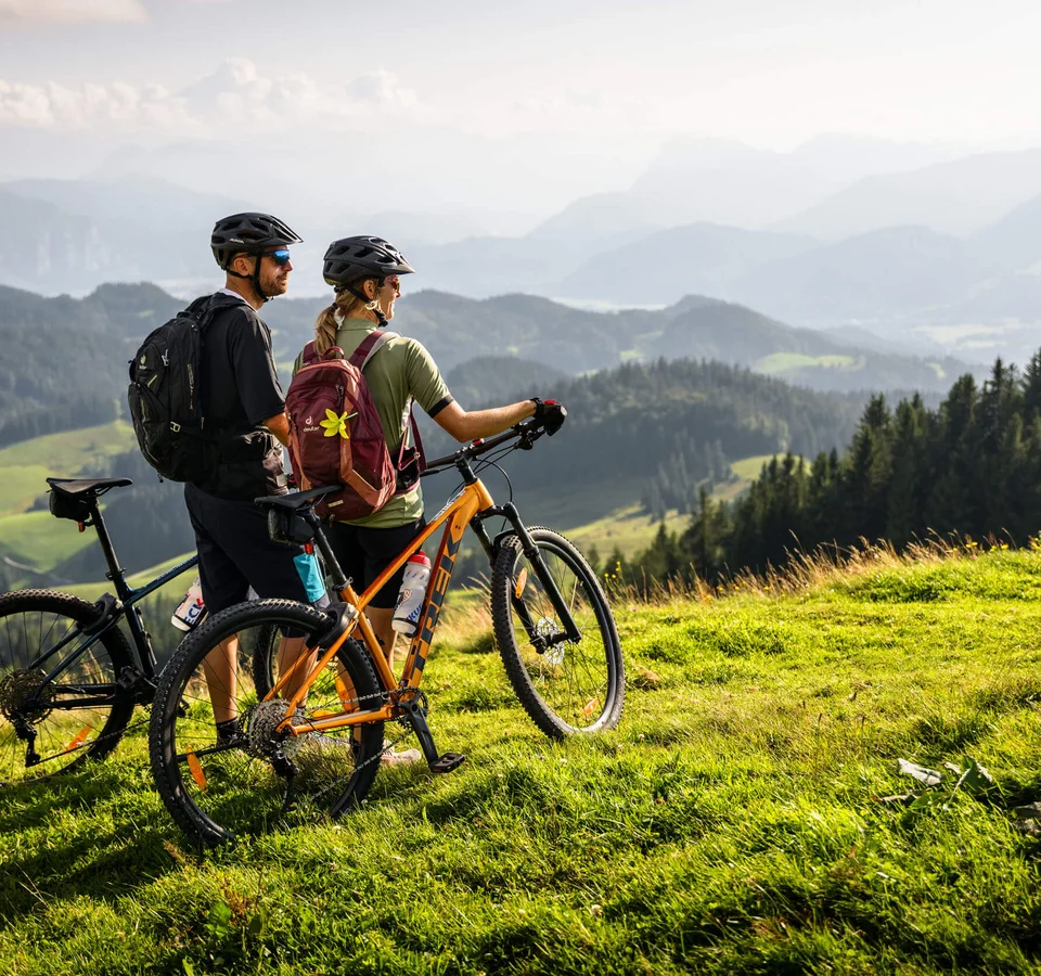 Zwei Radfahrer mit Helmen auf Bergwiese mit Blick auf Berge