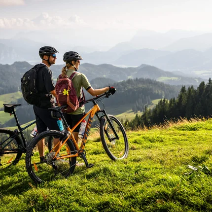 Zwei Radfahrer mit Helmen auf Bergwiese mit Blick auf Berge