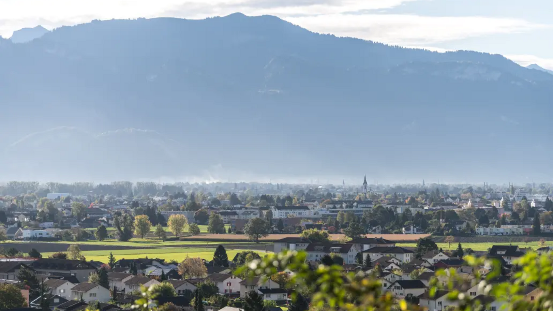 Town with houses and green fields in front of large misty mountains
