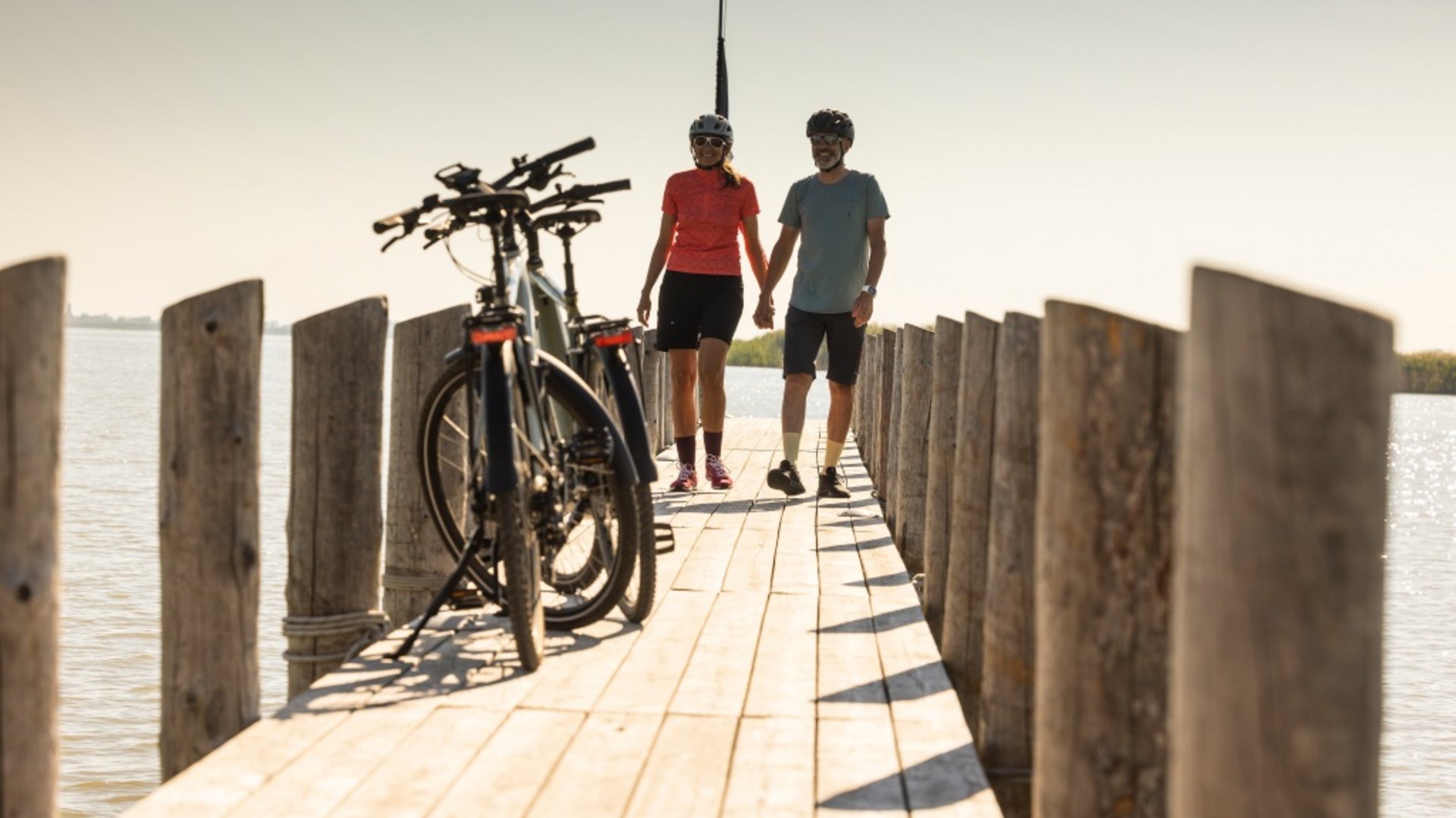 Couple with bicycles walking on a wooden pier by the water