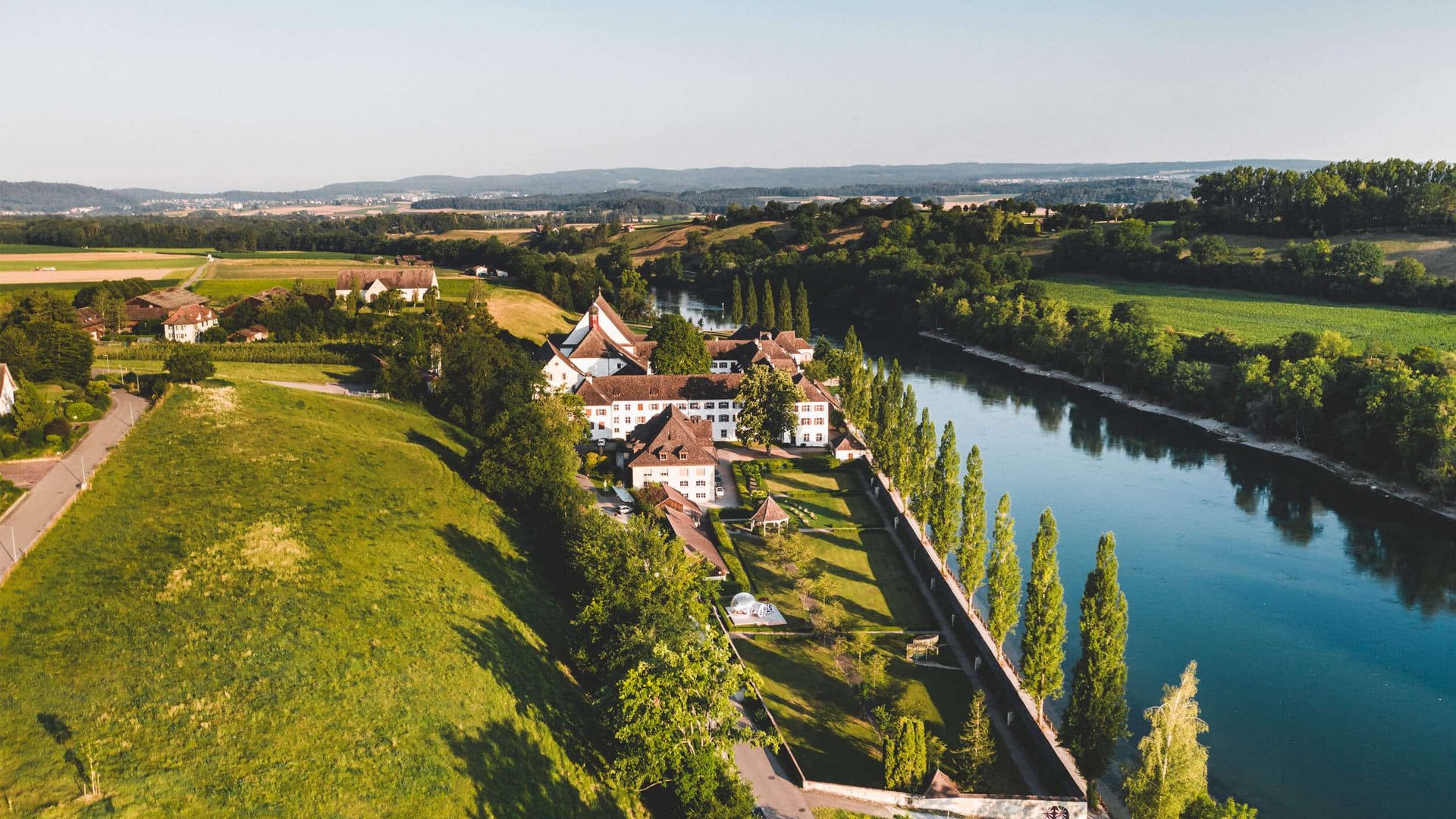 Aerial view of a castle by a river surrounded by green fields and trees