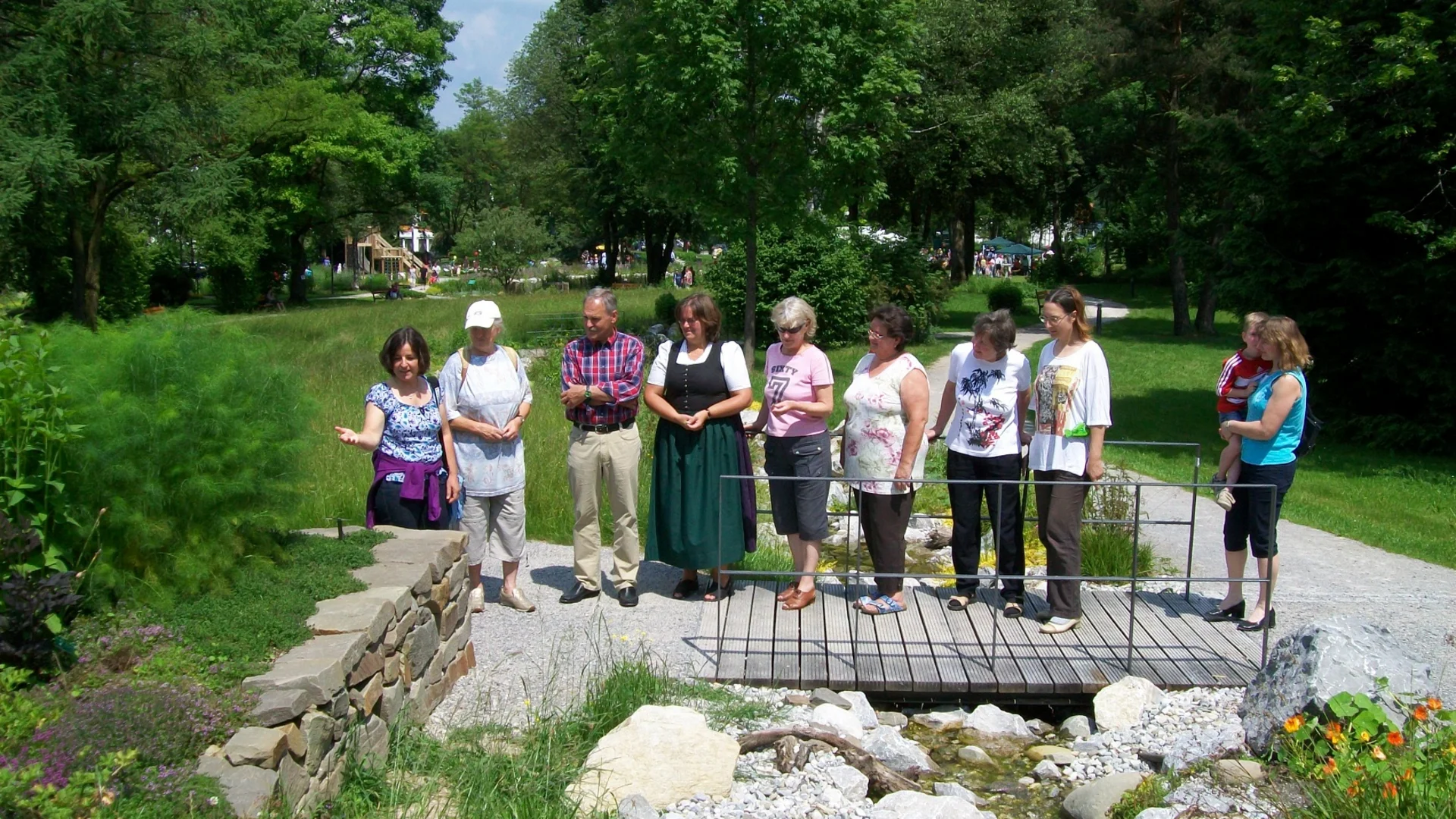 Gruppe von Menschen steht auf kleinem Steg im Park neben einem Felsenbach