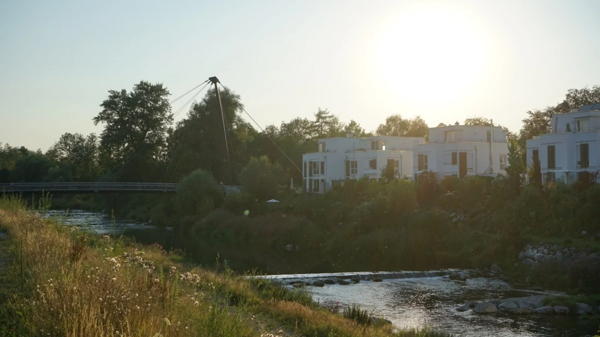 Sonnenuntergang über Fluss mit Brücke und modernen weißen Häusern