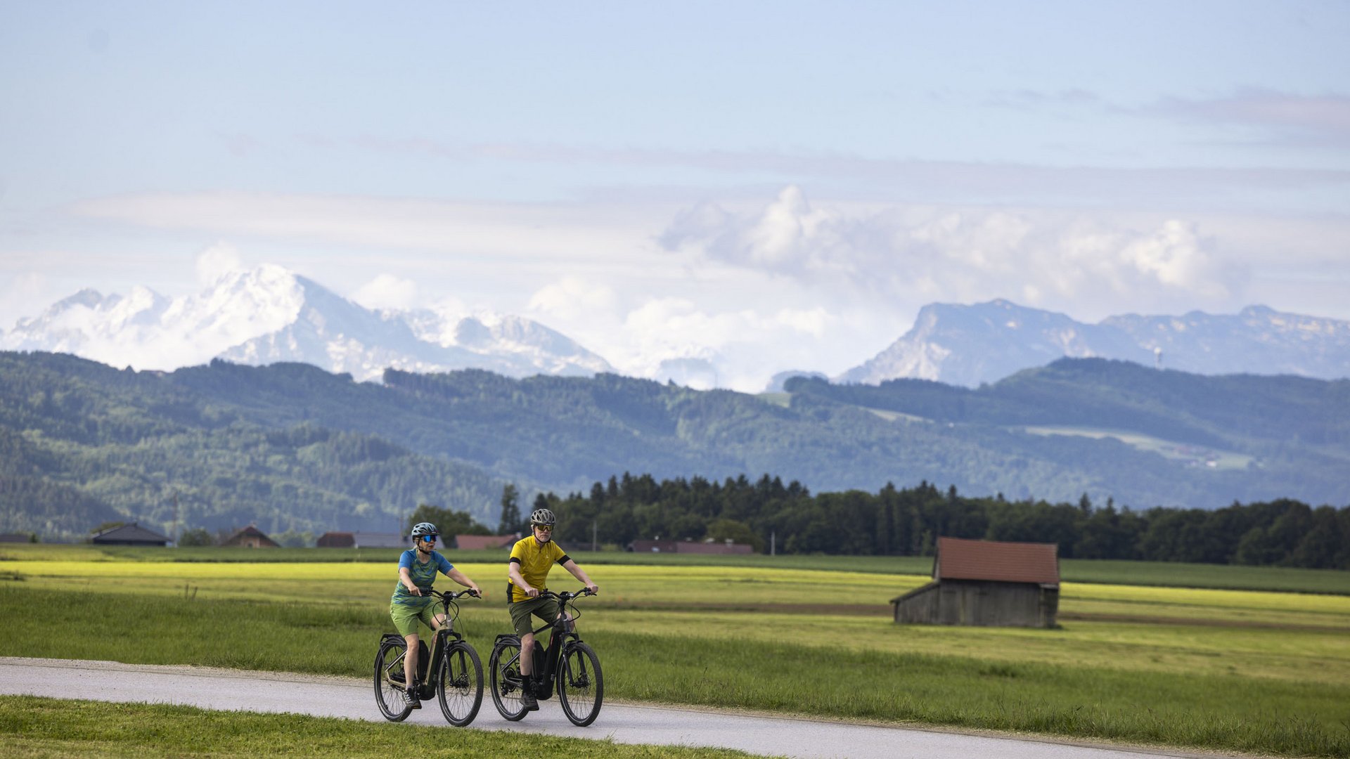 Two people cycling on a path in a mountainous countryside