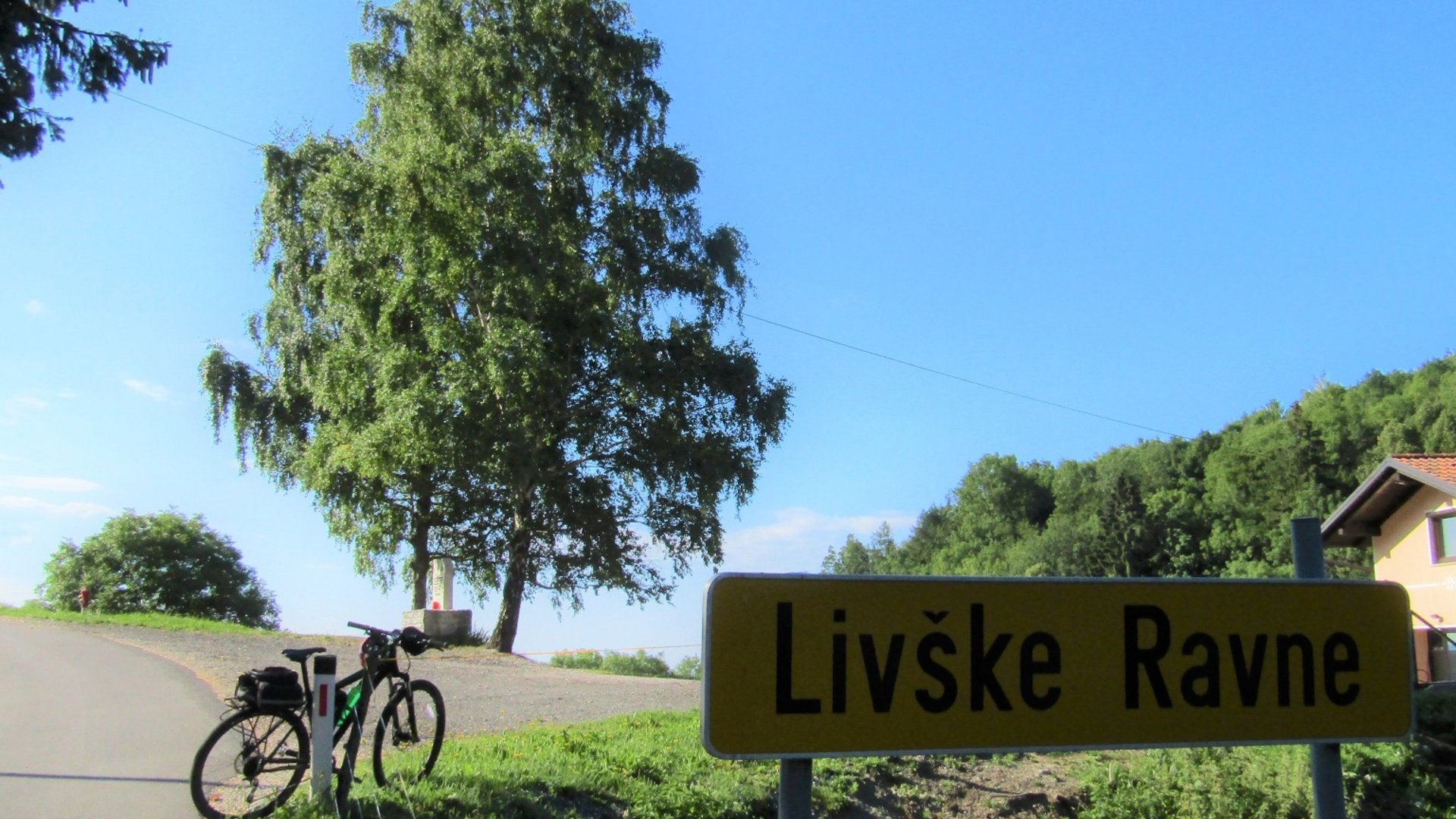 Bicycle next to Livške Ravne road sign under clear blue sky