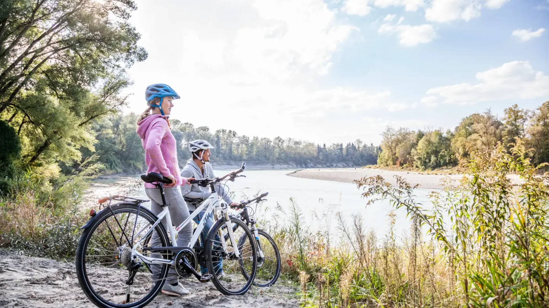 Zwei Radfahrer mit Helmen schauen auf einen Fluss in der Natur