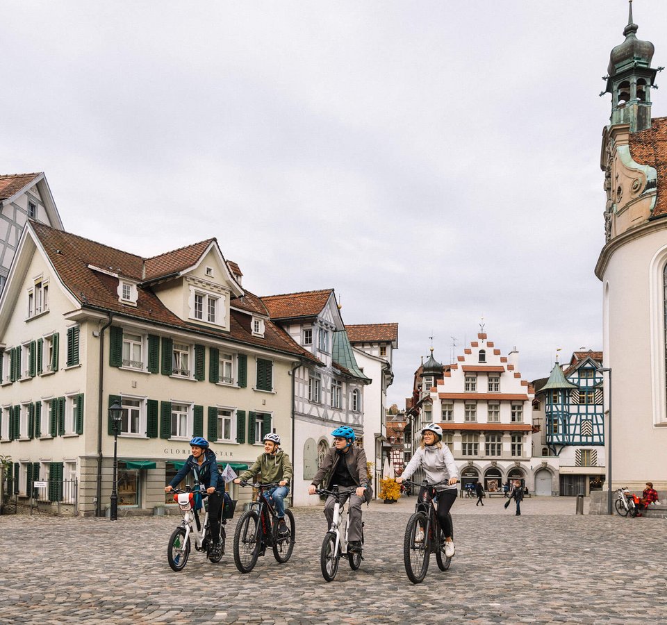 St.Gallen: Radurlaub im Herzen des UNESCO Welterbe © Giglio Pasqua Vier Personen fahren Fahrräder auf gepflastertem Platz vor historischen Gebäuden