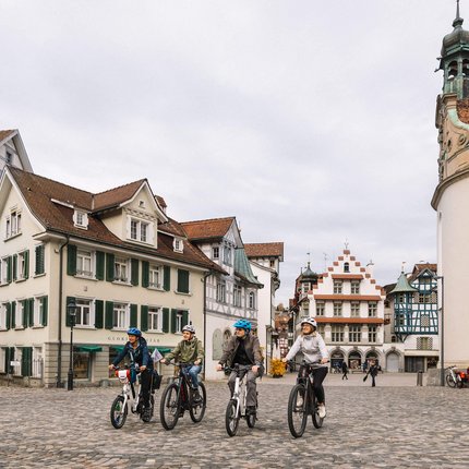 St.Gallen: Radurlaub im Herzen des UNESCO Welterbe © Giglio Pasqua Vier Personen fahren Fahrräder auf gepflastertem Platz vor historischen Gebäuden