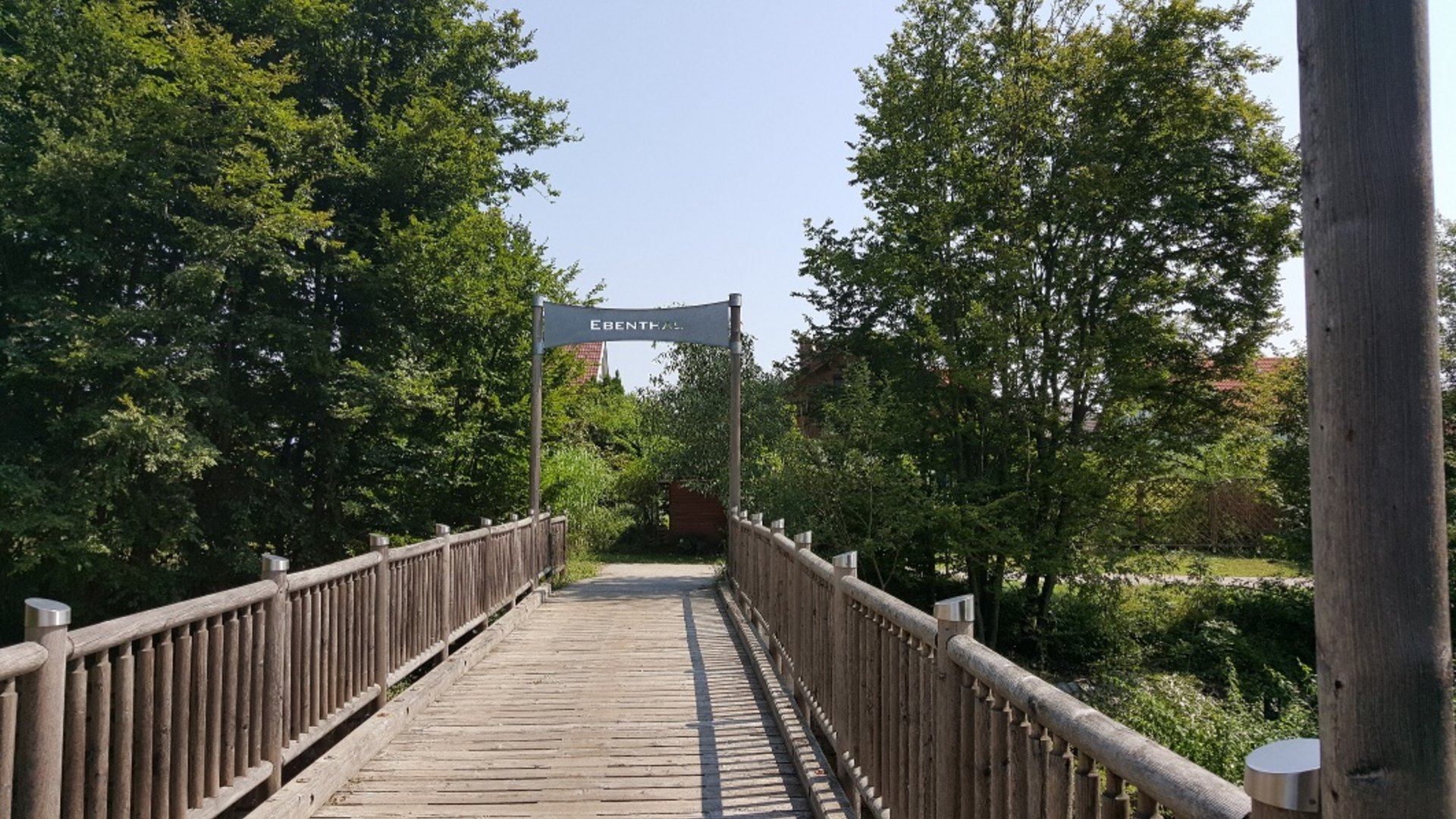 Wooden bridge with railing leading through green park in Ebenthal