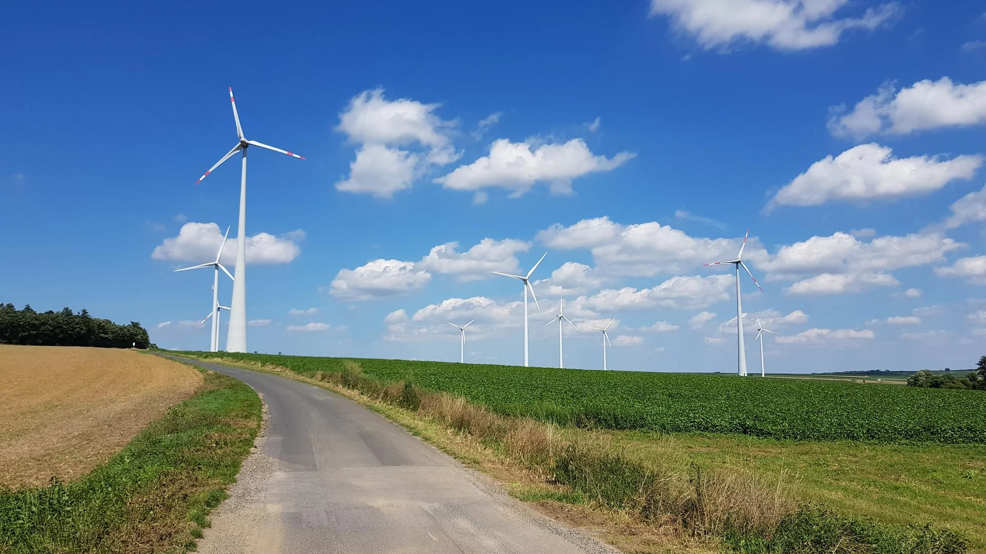 Landweg met windmolens onder blauwe lucht met wolken
