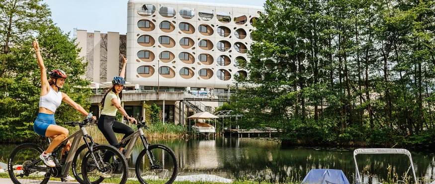 Twee vrouwen fietsen langs een meer bij een modern gebouw