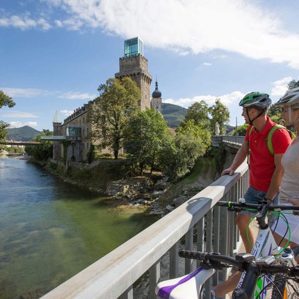 Cyclists on bridge looking at river and historic tower on sunny day
