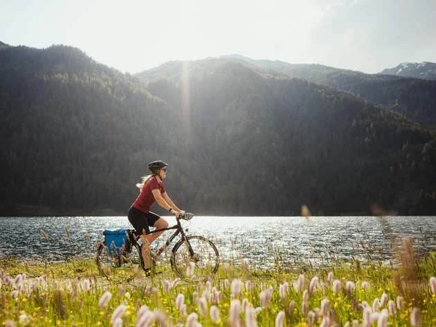 Drei Länder, du und dein Rad: Den Reschensee grenzüberschreitend entdecken © IDM Südtirol - Alex Moling Frau fährt Fahrrad am Seeufer mit Bergen im Hintergrund