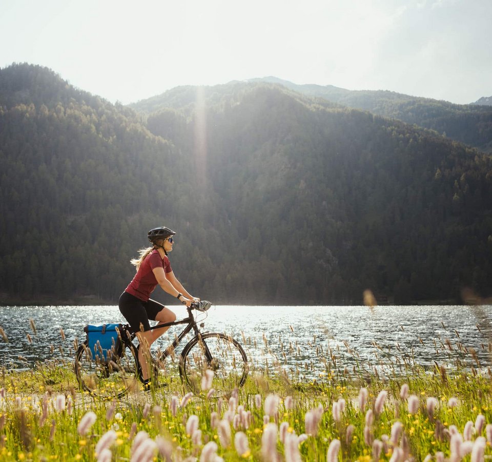 Frau fährt Fahrrad am Seeufer mit Bergen im Hintergrund