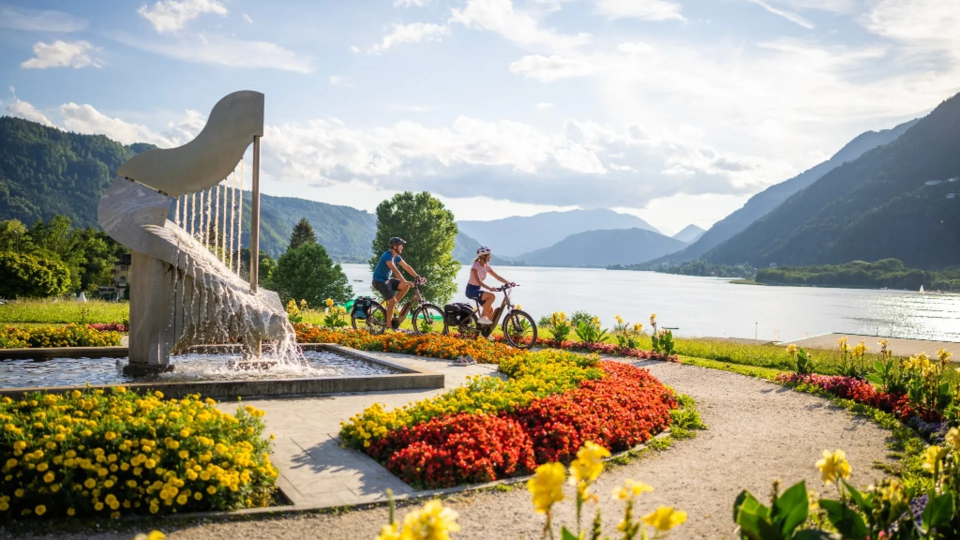 Fietsers rijden langs een bloemrijk pad aan het meer met bergen op de achtergrond