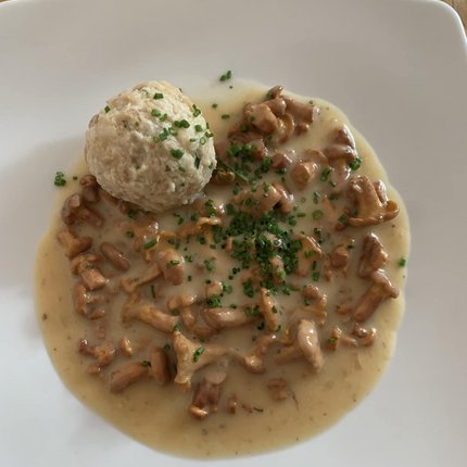 Bread dumpling with creamy chanterelles and chives on white plate