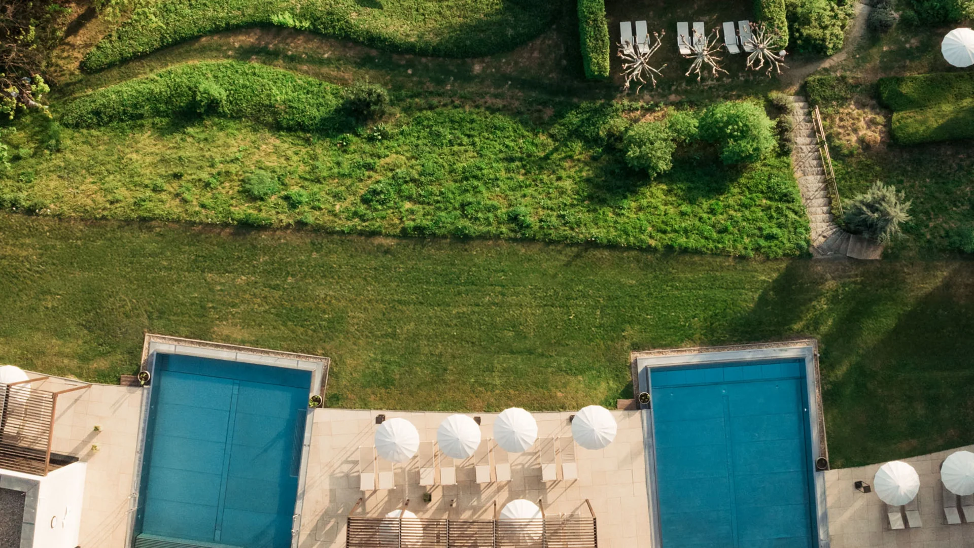 Top view of two pools and sun loungers by a green garden