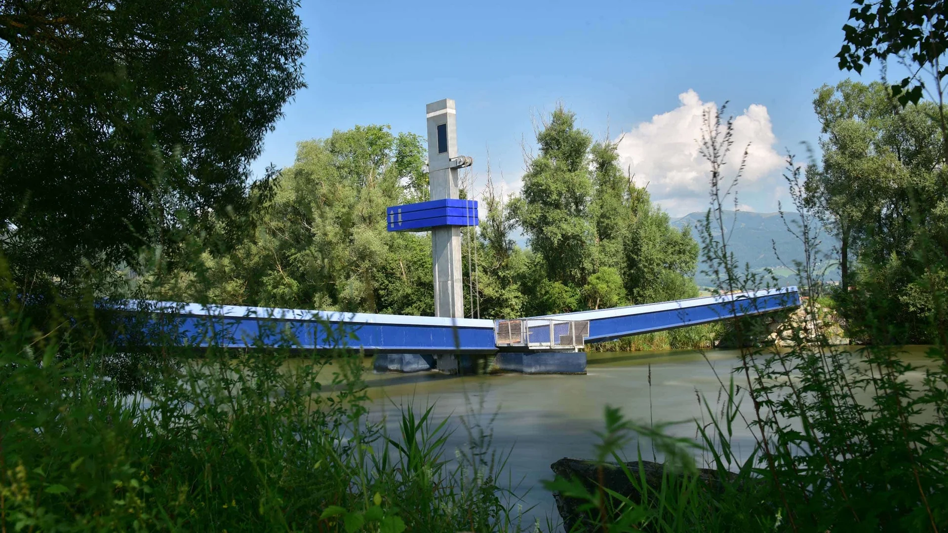 Blauwe ophaalbrug over een rivier, omgeven door bomen en begroeiing