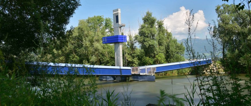 Blue drawbridge over a river, surrounded by trees and vegetation